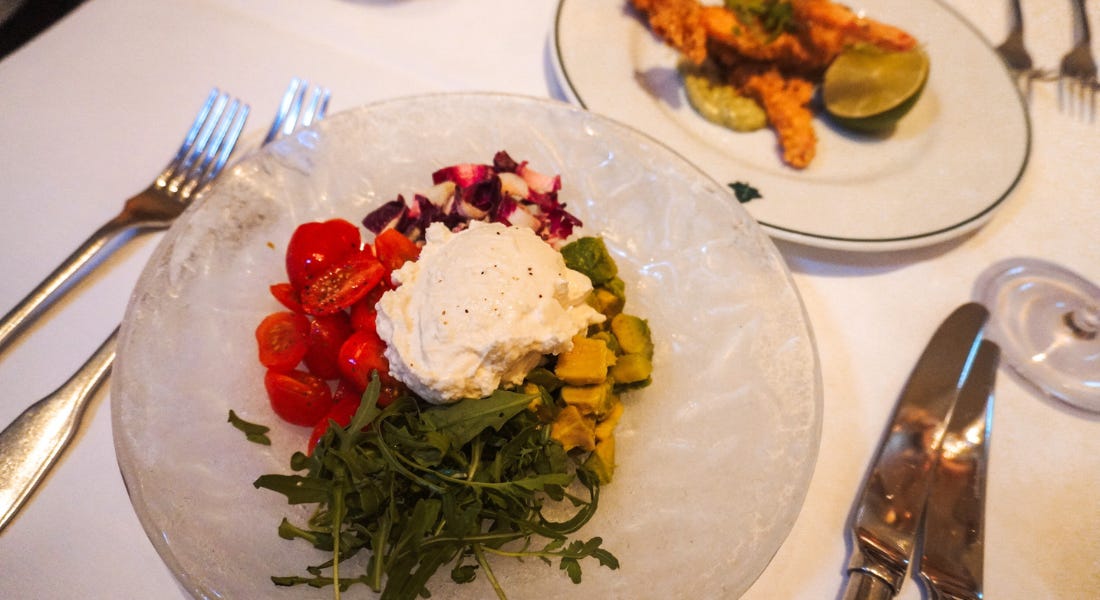 Two plates - one with a cheese and tomato salad and one with prawns, with cutlery either side and a white tablecloth Two plates - one with a cheese and tomato salad and one with prawns, with cutlery either side and a white tablecloth