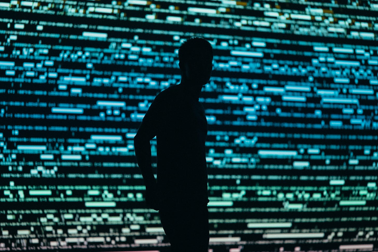 silhouette of a person standing in front of a giant computer screen with green and blue dashed lines and symbols silhouette of a person standing in front of a giant computer screen with green and blue dashed lines and symbols