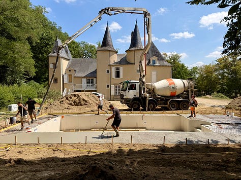 Pool construction at the château, with a concrete truck pouring beside the towers, a pool shell with pipes, and a trench of electrical cable;