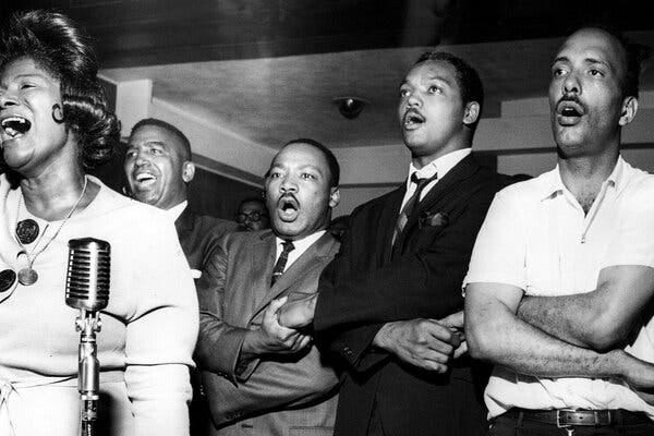 A group of men including Jesse Jackson and Dr. King hold hands and sing behind Mahalia Jackson.