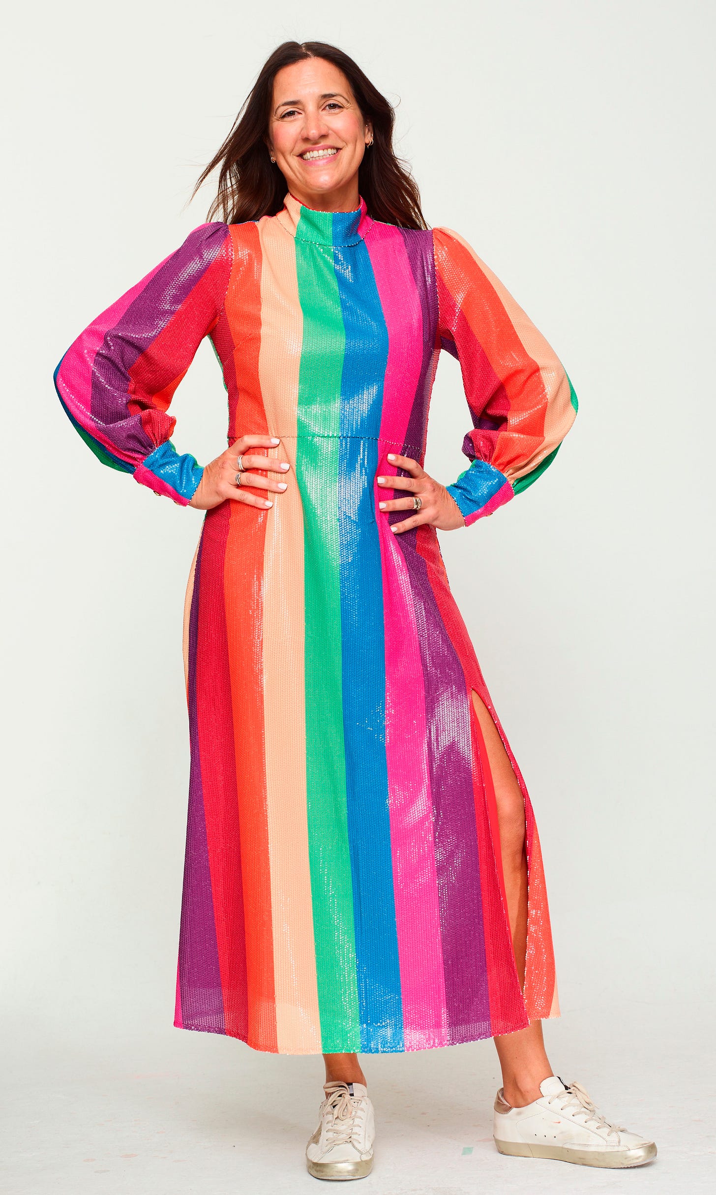 A smiling professional beauty editor with long brown hair, wearing a white button-down shirt, posed against a neutral, light-wood paneled background.