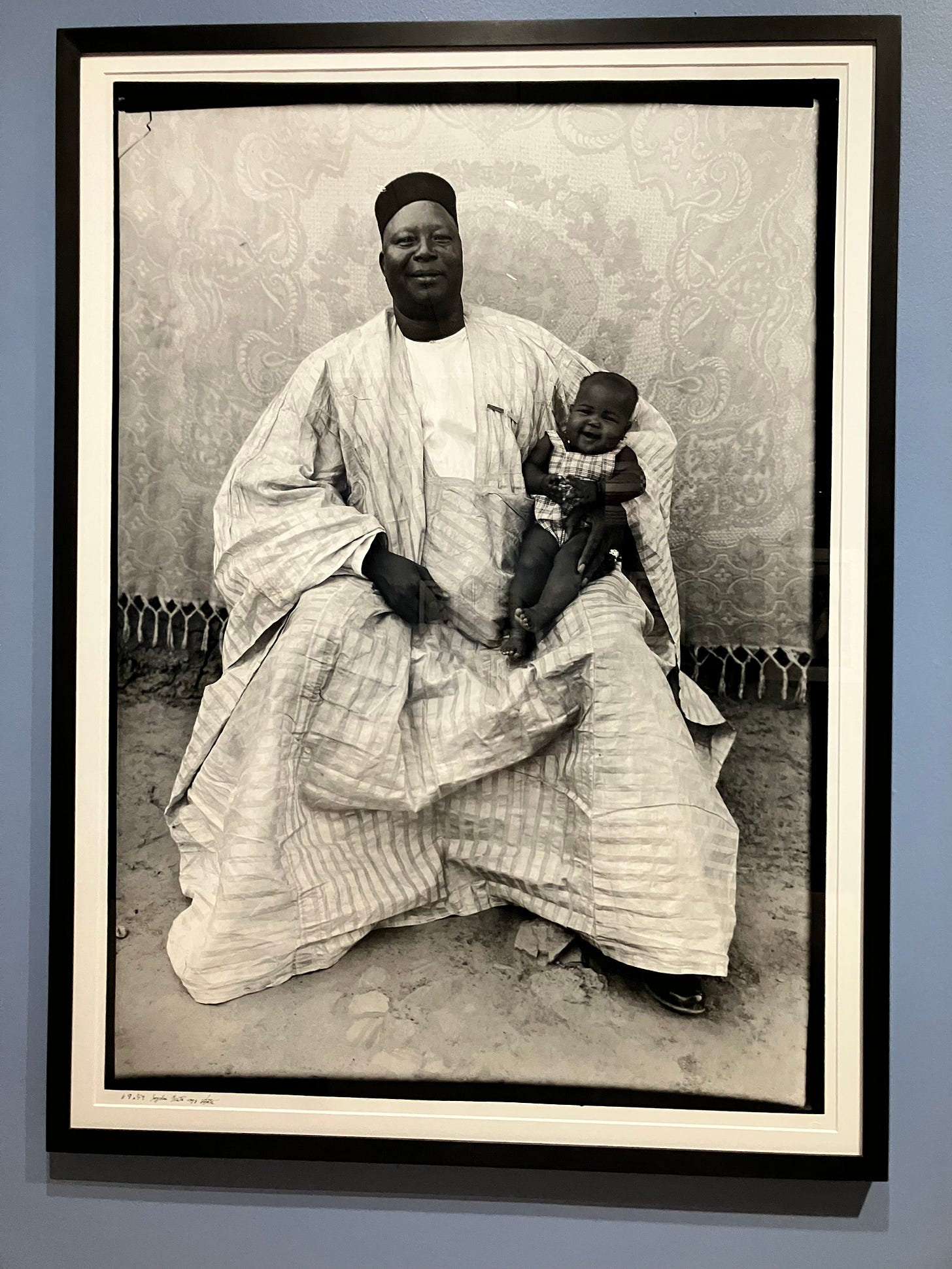 Photograph of a large African man in a striped robe holding a small boy on his lap. Photograph of a large African man in a striped robe holding a small boy on his lap.