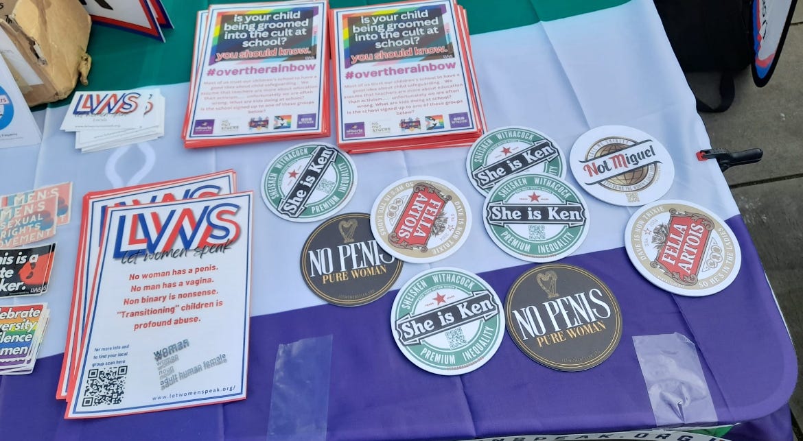Action shot of a diverse group of women engaging passersby at a locals table during a natural daylight community outreach event.