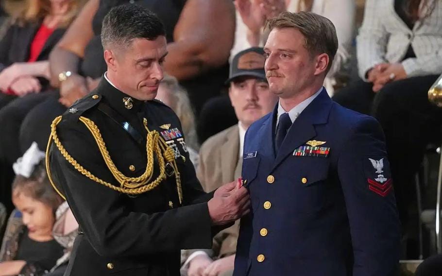 A man in a gray-green uniform pins a medal on a man in a blue uniform. A man in a gray-green uniform pins a medal on a man in a blue uniform.