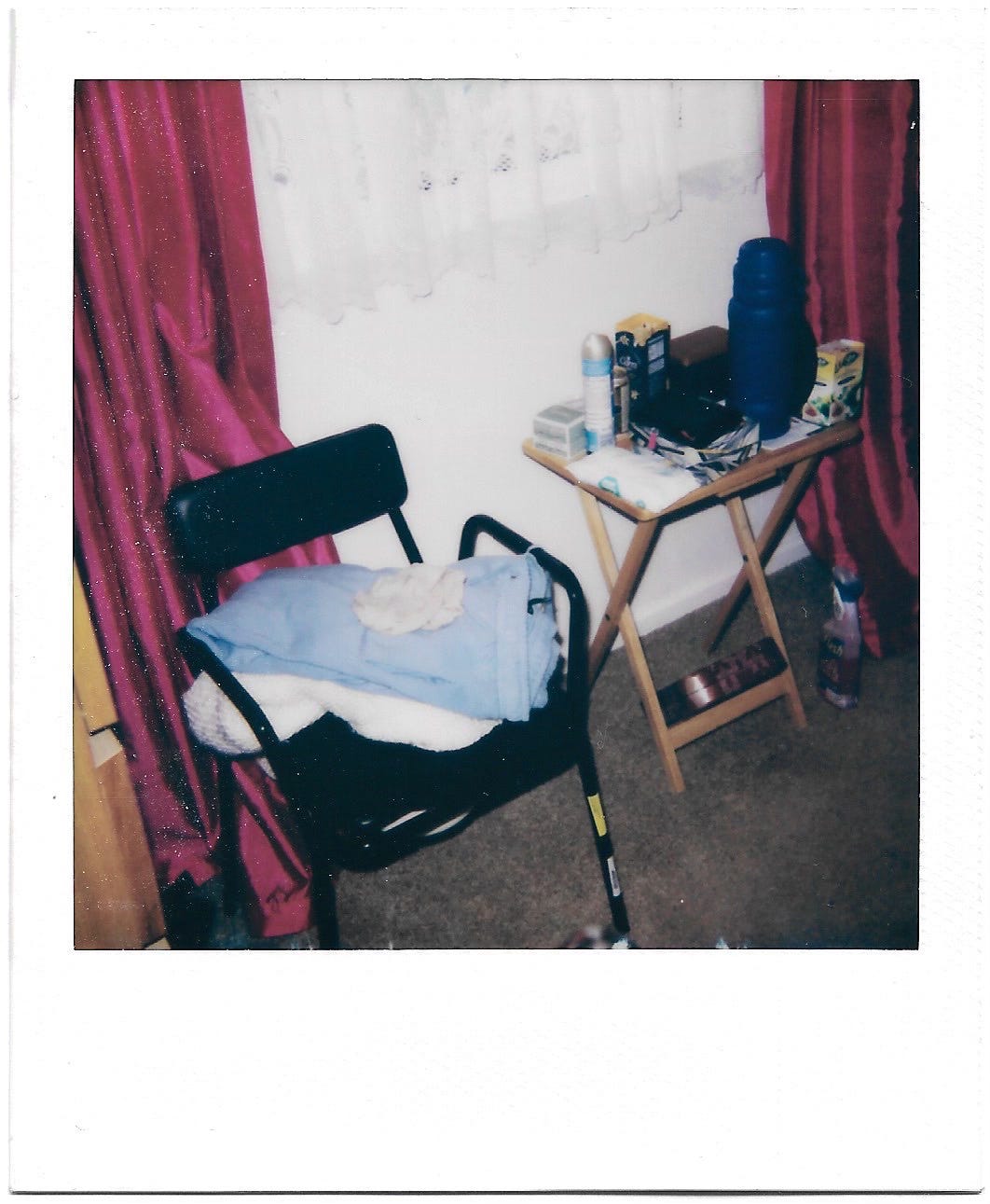 A colour Polaroid photograph of a bedroom, containing a commode and assorted