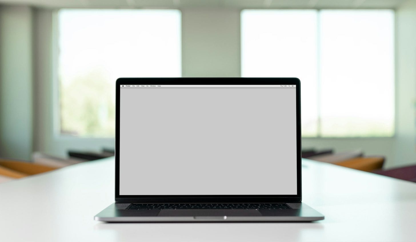 An open laptop on a white table in a bright office, its screen showing an empty gray browser window.