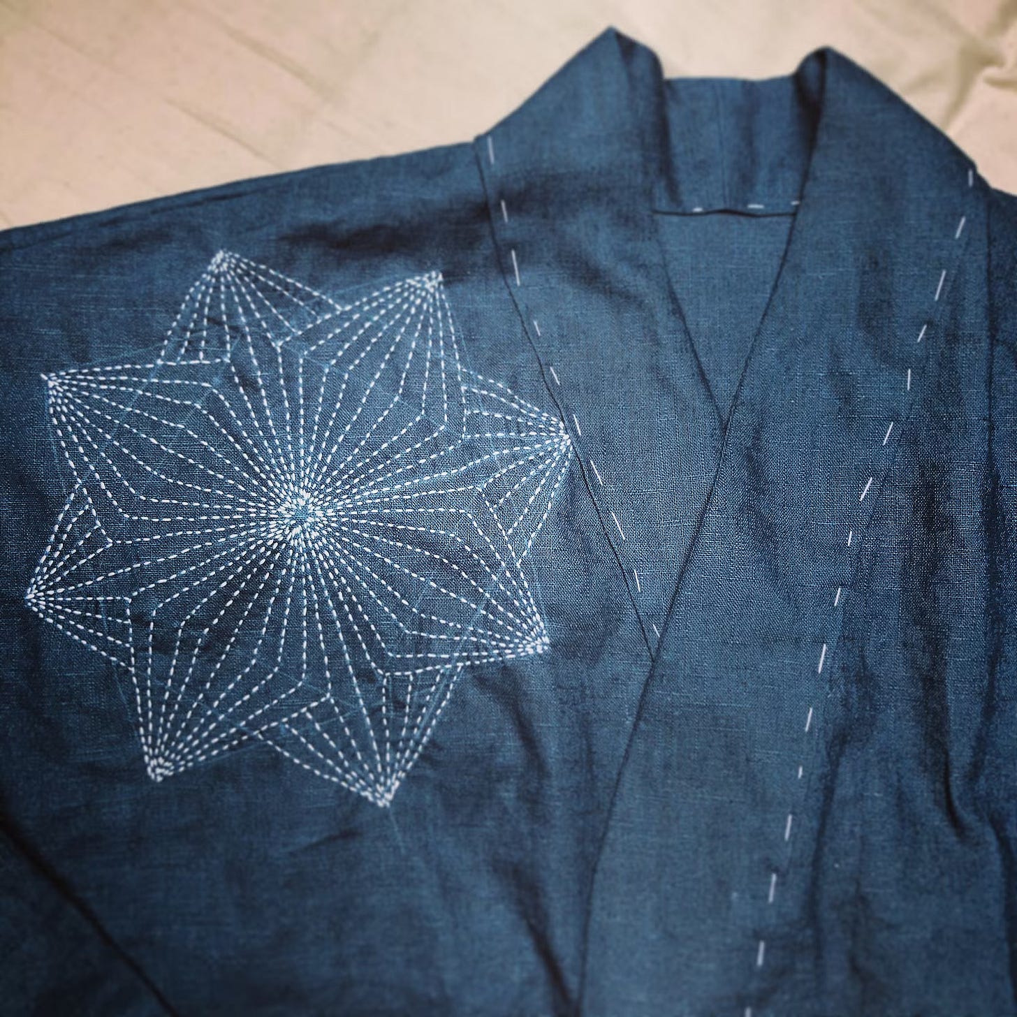 A indigo blue shirt with white stitching on the collar and a white stitched geometric star/flower pattern on the left shoulder.