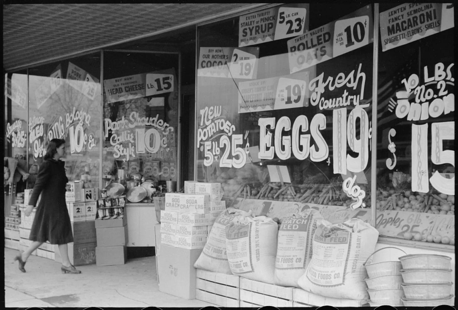 Salem, Illinois grocery store, 1940. Every inch of window space used for hand-lettered price signs — the price always the largest element. Library of Congress.