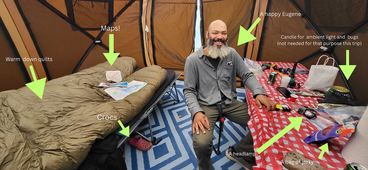 A candid interior view of a large camping tent. Eugene sits in a camp chair, smiling, next to a table and a cot where a topographical map is spread out. Hand-written style text overlays point out various essential gear and supplies organized throughout the space.
