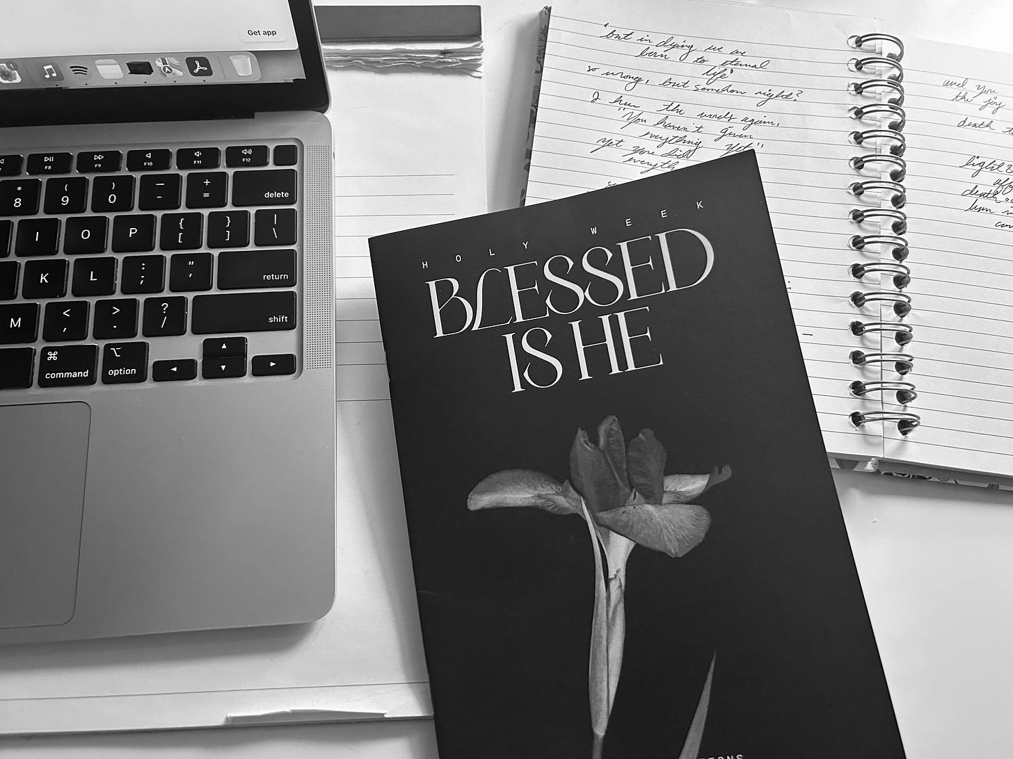 Picture shows a journal open with a prayer, a book with the cover reading "blessed is he" and a laptop all in black in white Picture shows a journal open with a prayer, a book with the cover reading "blessed is he" and a laptop all in black in white
