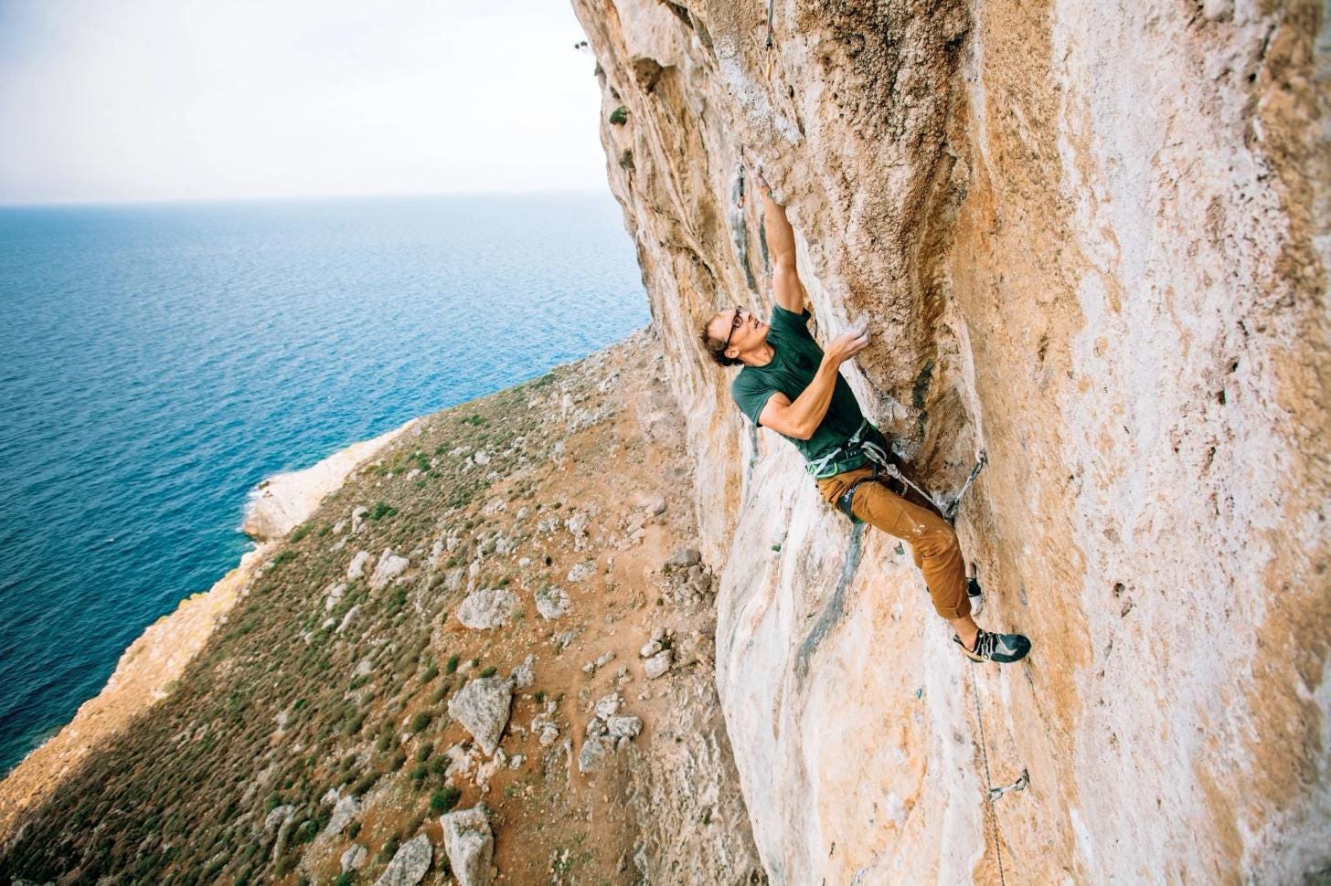 A climber ascending an easy limestone route on Kalymnos Island, Greece, with views of the Aegean Sea in the background. A climber ascending an easy limestone route on Kalymnos Island, Greece, with views of the Aegean Sea in the background.