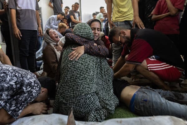 A woman hugs another woman amid a group of people crying and wailing.