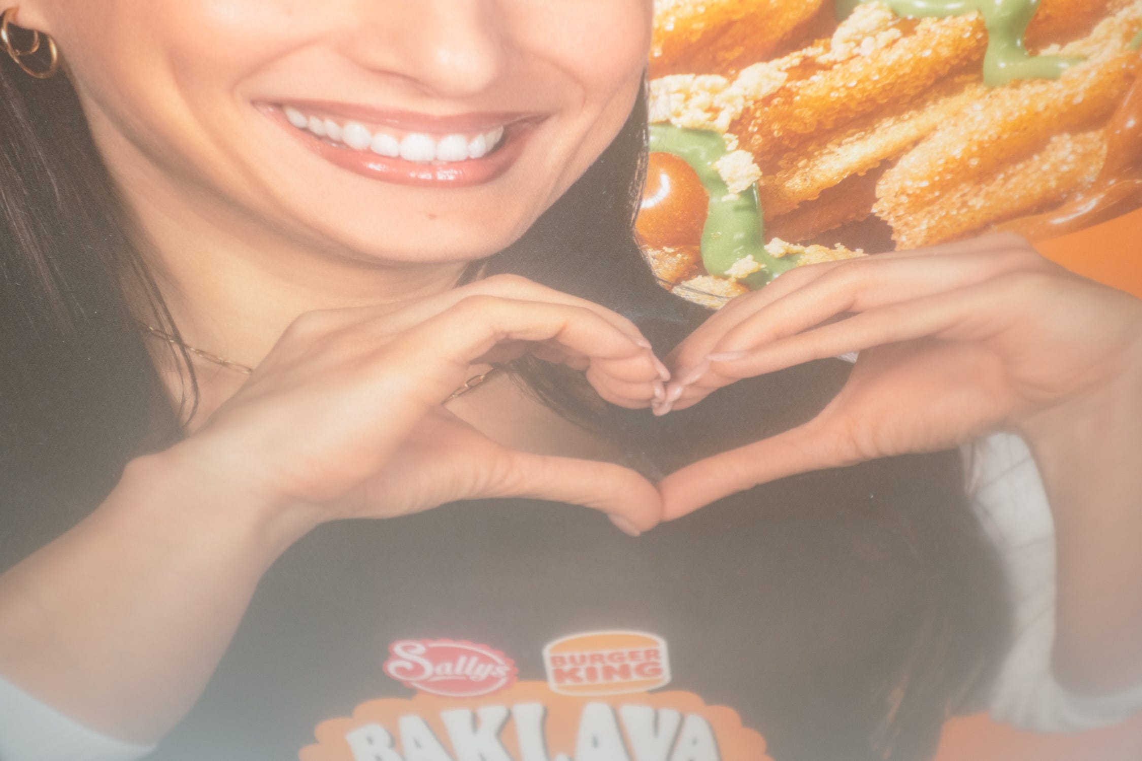 A close-up of a smiling woman in an advertisement making a heart shape with her hands in front of a fast-food meal.