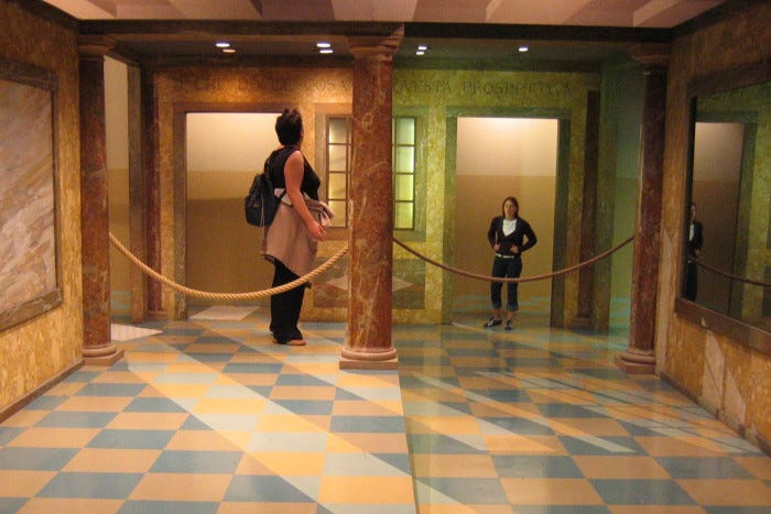 Picture of two people standing in an Ames room. They appear physically very different in size (left: larger) and the only clue to this artefact is that the spanning rope on the right is narrower because it's more distant. Picture of two people standing in an Ames room. They appear physically very different in size (left: larger) and the only clue to this artefact is that the spanning rope on the right is narrower because it's more distant.