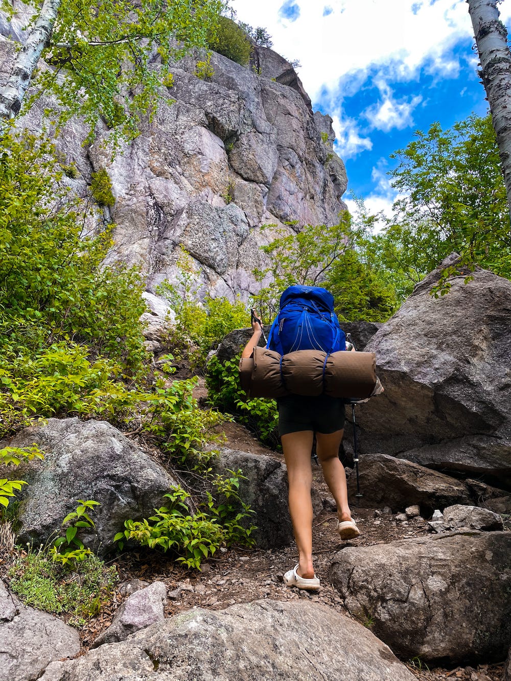 Picture shows Lisa in crocs hiking up a boulder with her blue hiking pack. Picture shows Lisa in crocs hiking up a boulder with her blue hiking pack.