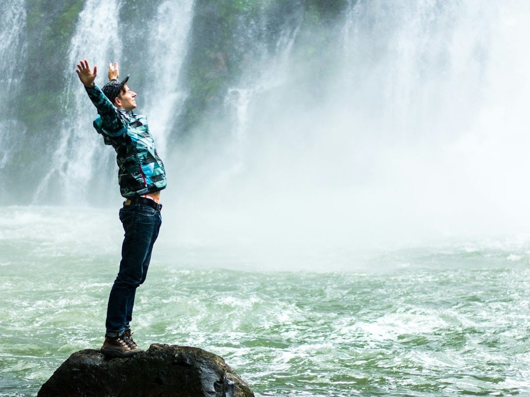 man standing on black rock surrounded body of water