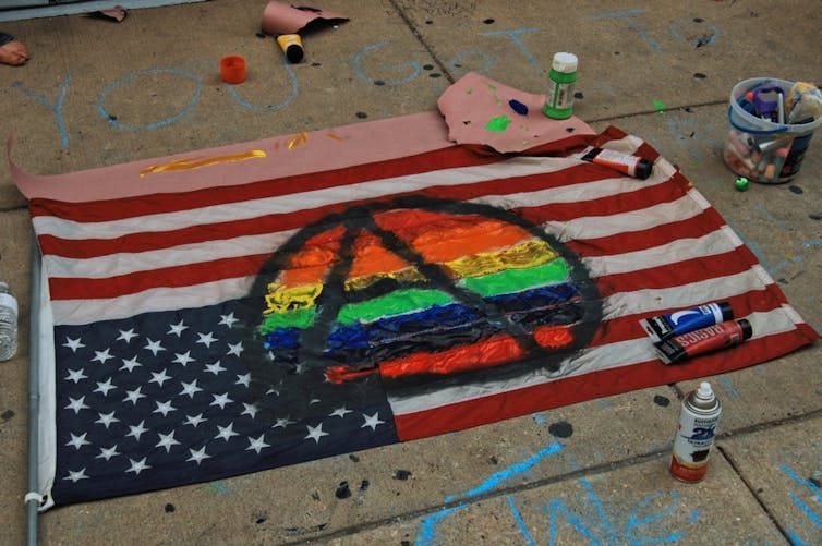 American flag on ground painted over with rainbow-filled anarchist symbol