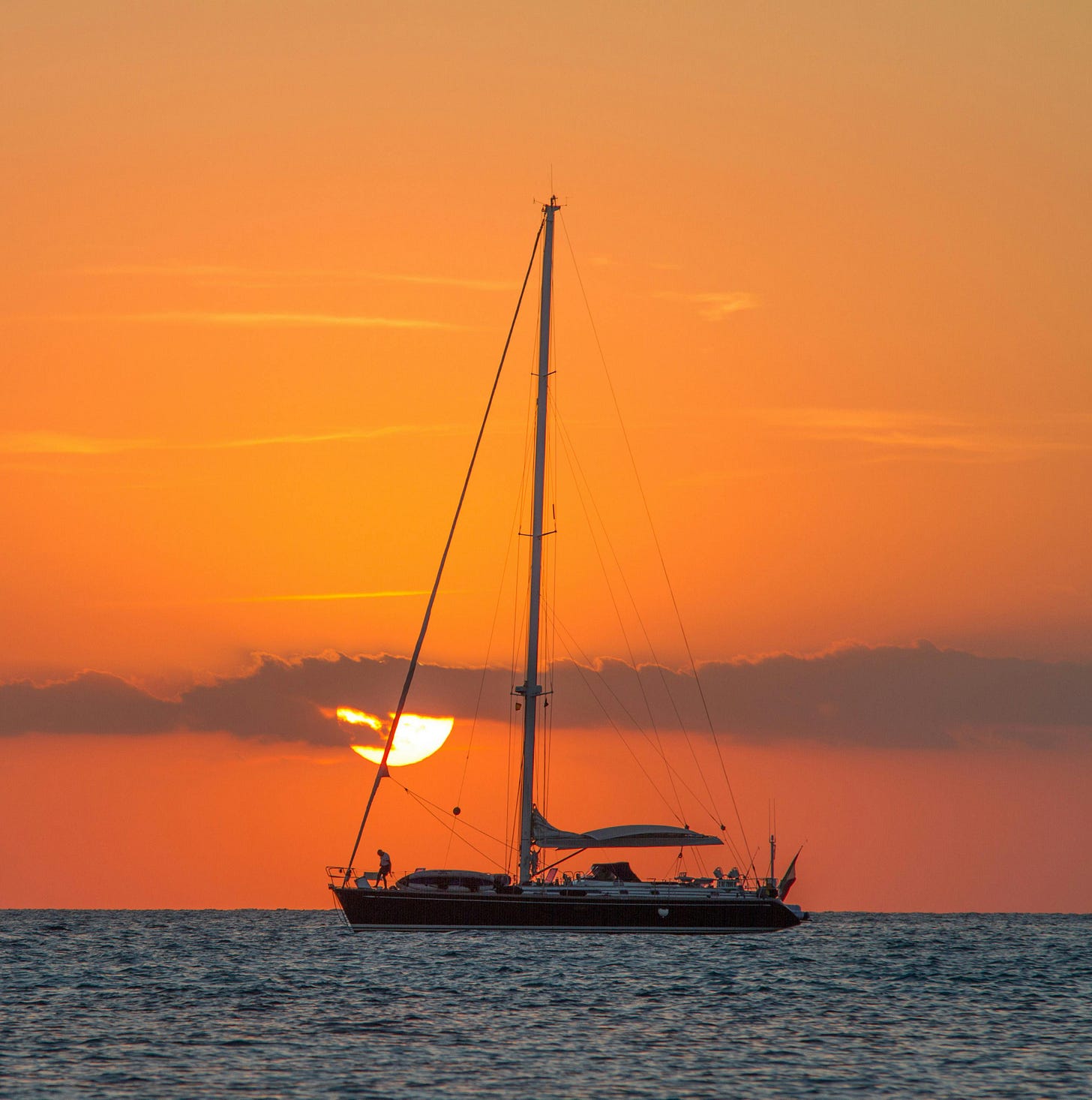 Free A sailboat glides across the sea against a vibrant sunset near the Balearic Islands. Stock Photo
