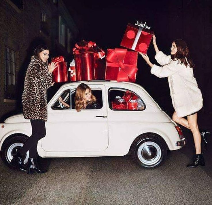 This may contain: two beautiful women standing next to a white car with presents on the hood and back