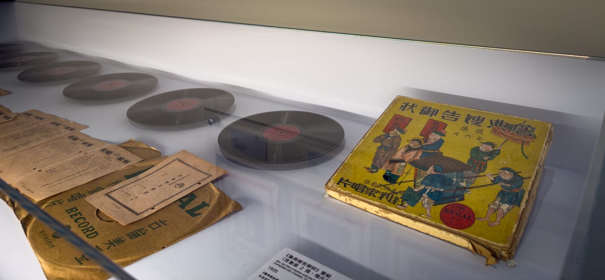 On the right, a colorful record case sits at the base of a row of black records stretching out of the frame to the left