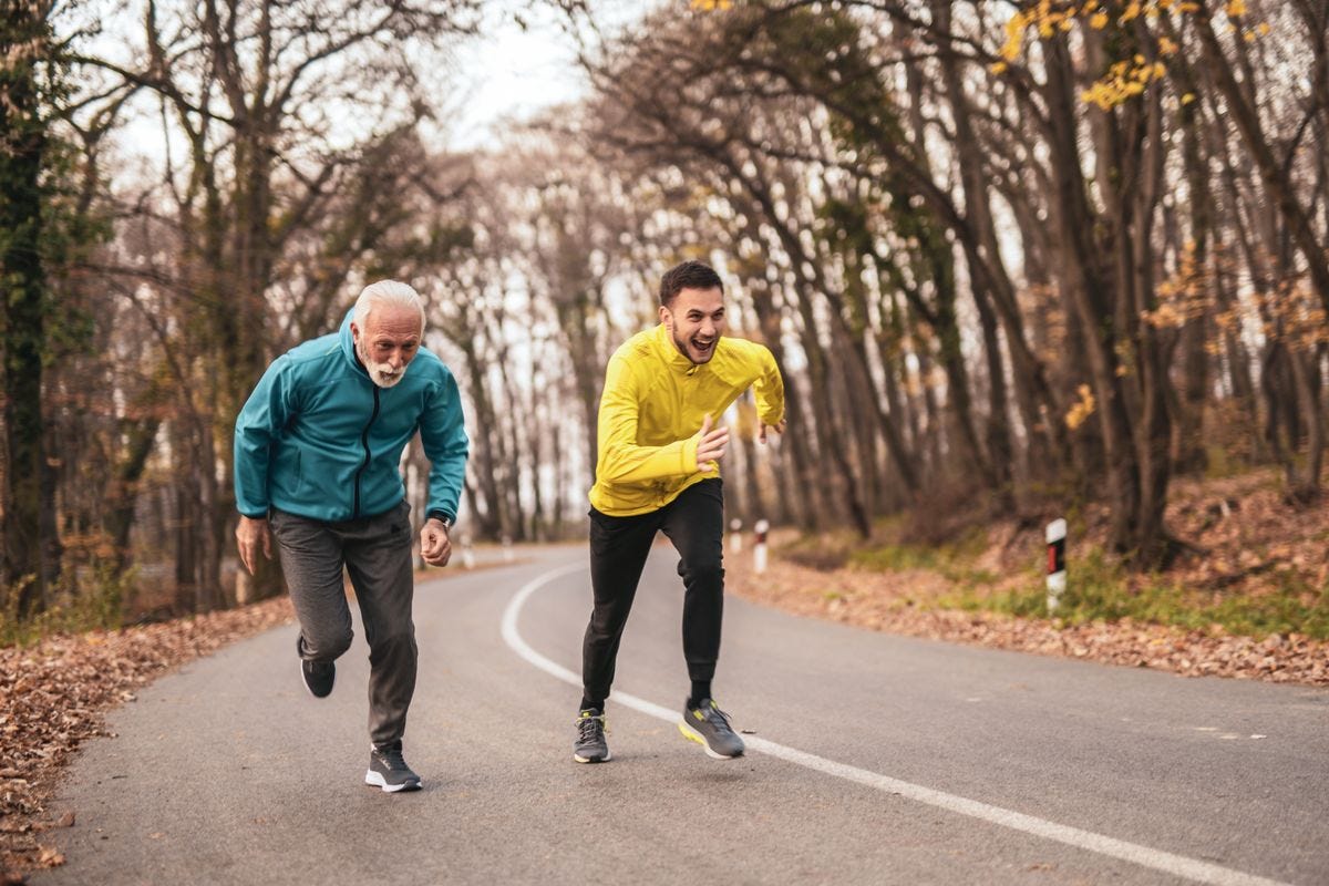 Senior man and his son running together on scenic road.