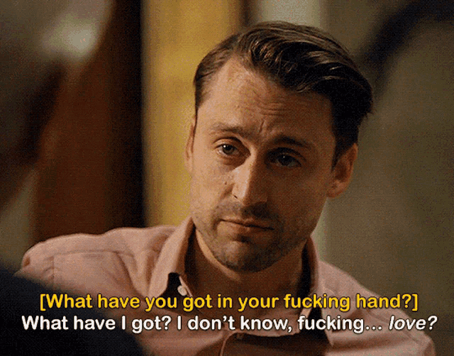 a man in a pink shirt is talking to another man and says what have you got in your fucking hand