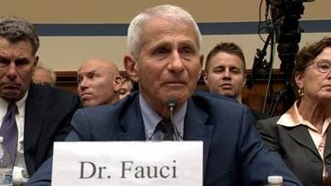 Dr. Anthony Fauci sits at a witness table during a congressional hearing, with a Dr. Fauci nameplate visible in front of him. 
