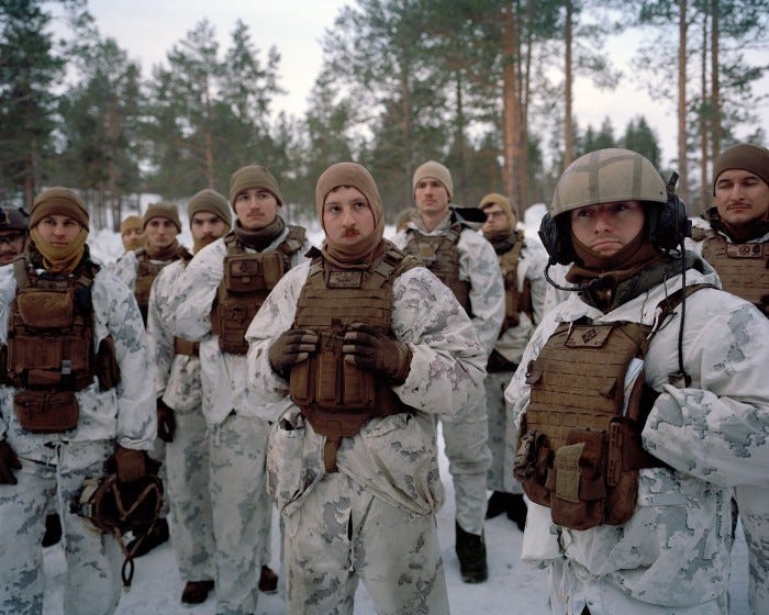 A group of soldiers in full snow combat gear stand listening. In the background we see tall pines and snow. They are being debriefed after a training in driving on ice A group of soldiers in full snow combat gear stand listening. In the background we see tall pines and snow. They are being debriefed after a training in driving on ice