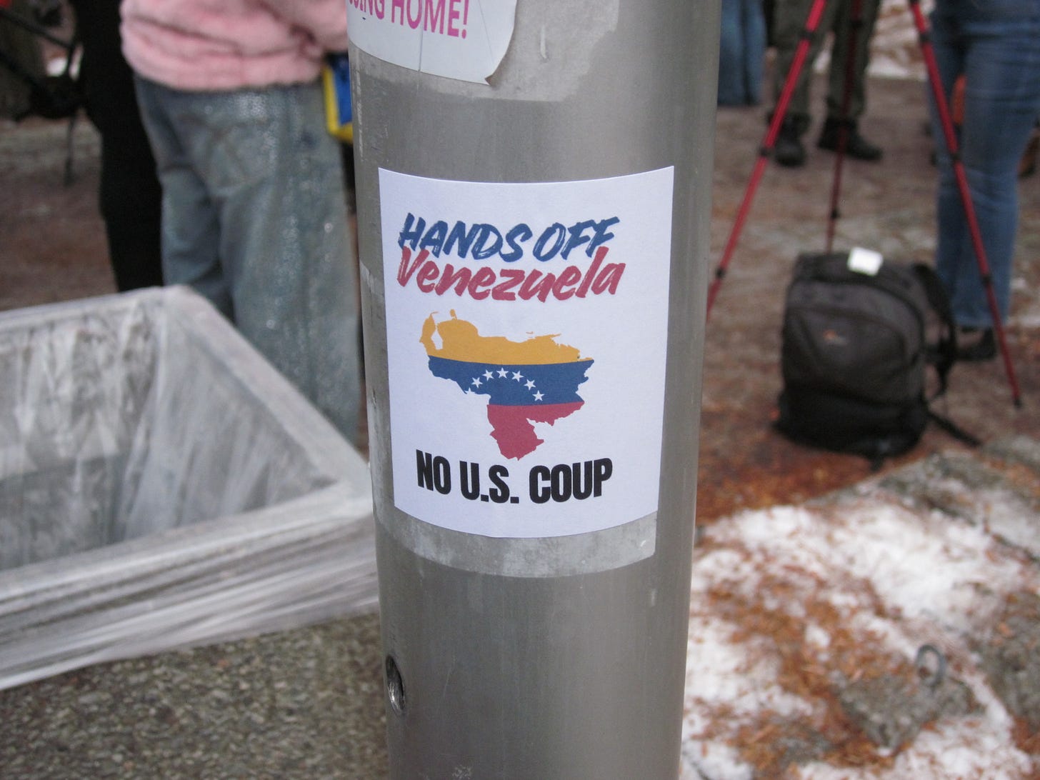 A pole with a sticker featuring the Venezuelan state map and flag design and the text “Hands Off Venezuela. No US Coup.” A pole with a sticker featuring the Venezuelan state map and flag design and the text “Hands Off Venezuela. No US Coup.”