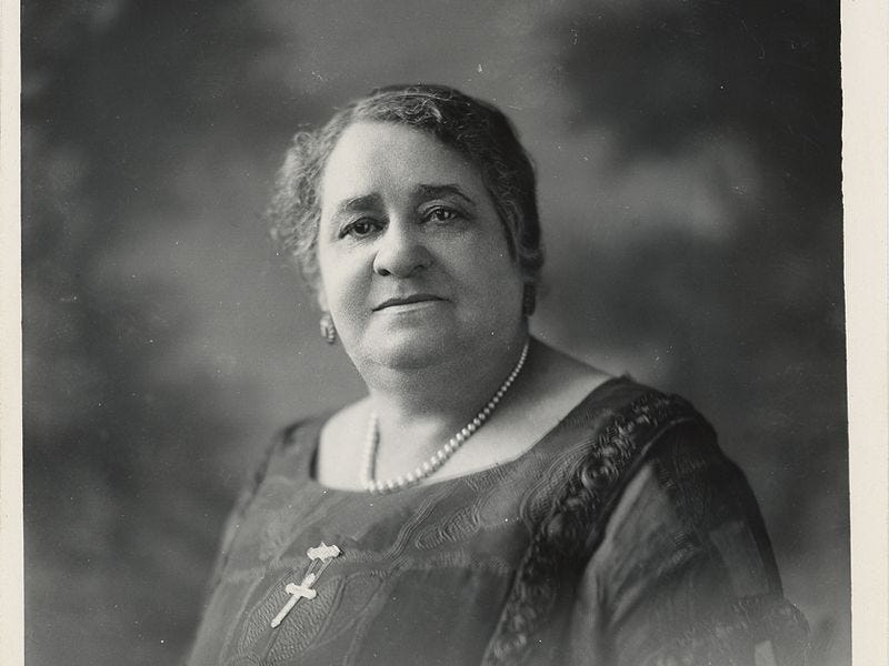 A black and white photo of Maggie Lena Walker, a Black woman, wearing a black dress and a crucifix necklace A black and white photo of Maggie Lena Walker, a Black woman, wearing a black dress and a crucifix necklace