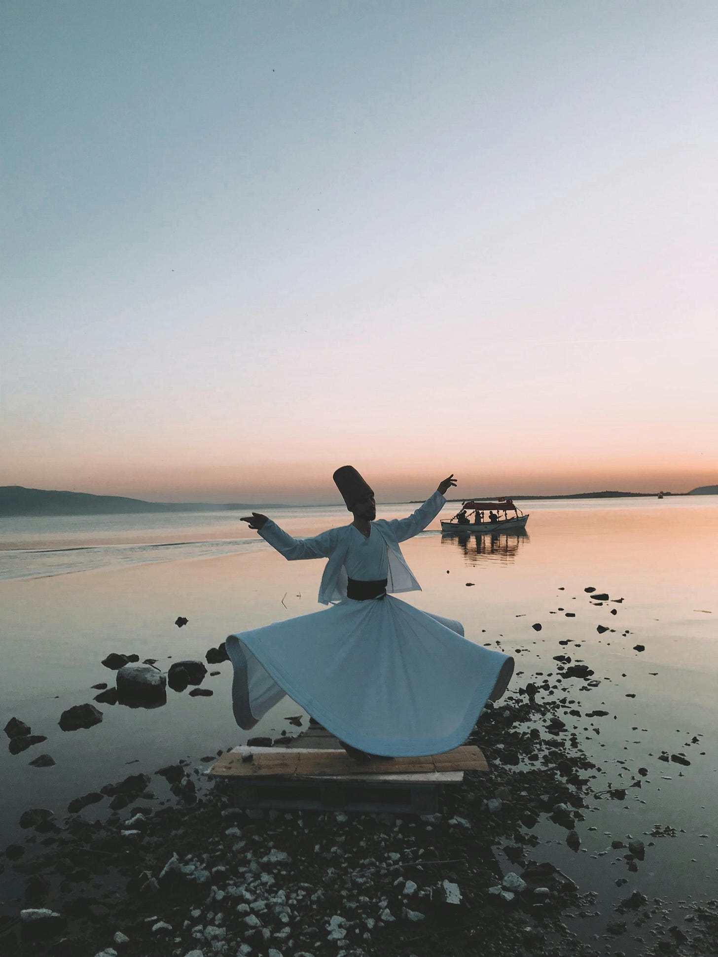 Dancing Whirling Dervish on Pebbles and Boat on Lake at Dusk, Nilüfer, Bursa, Turkey, June 20, 2021 by Leo Arslan.