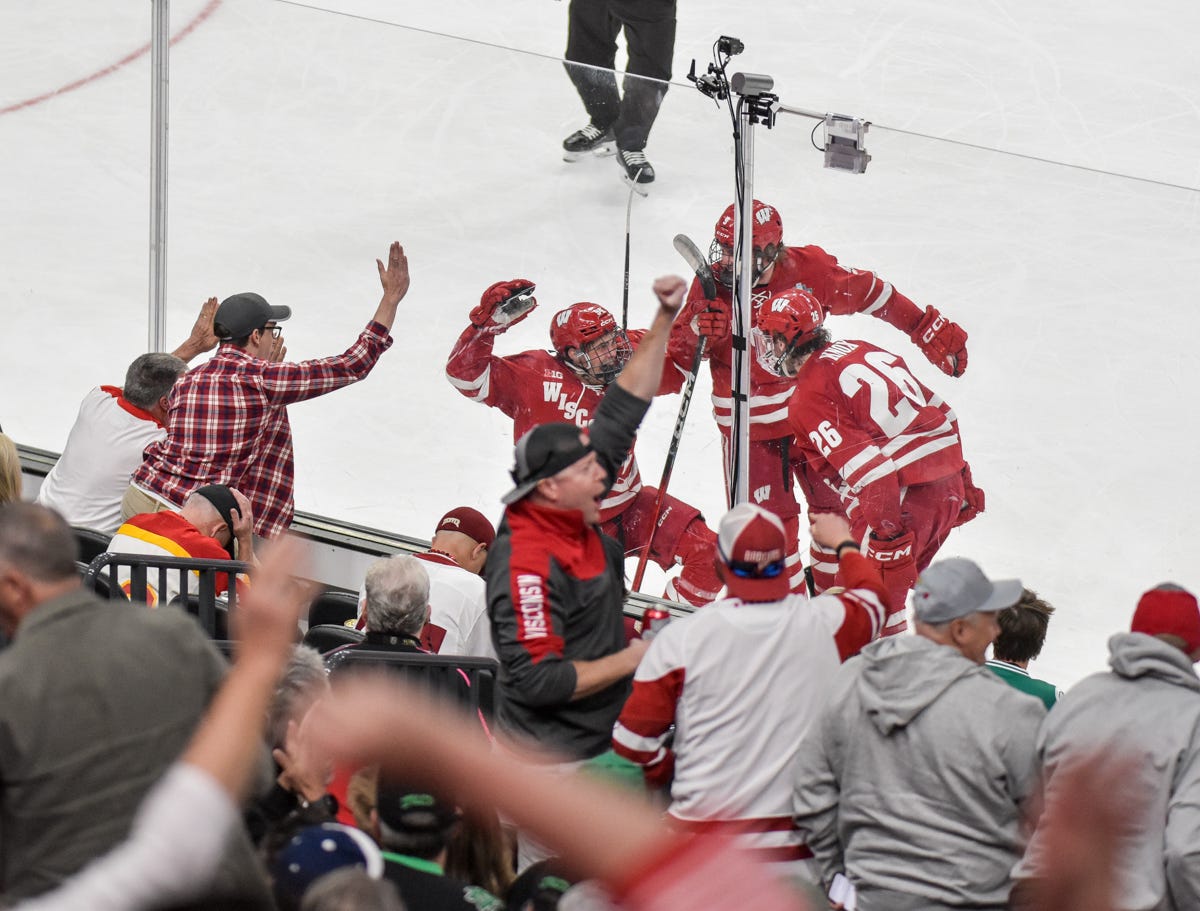 Wisconsin freshman Vasily Zelenov celebrates with teammates in front of glass while fans cheer at T-Mobile Arena.