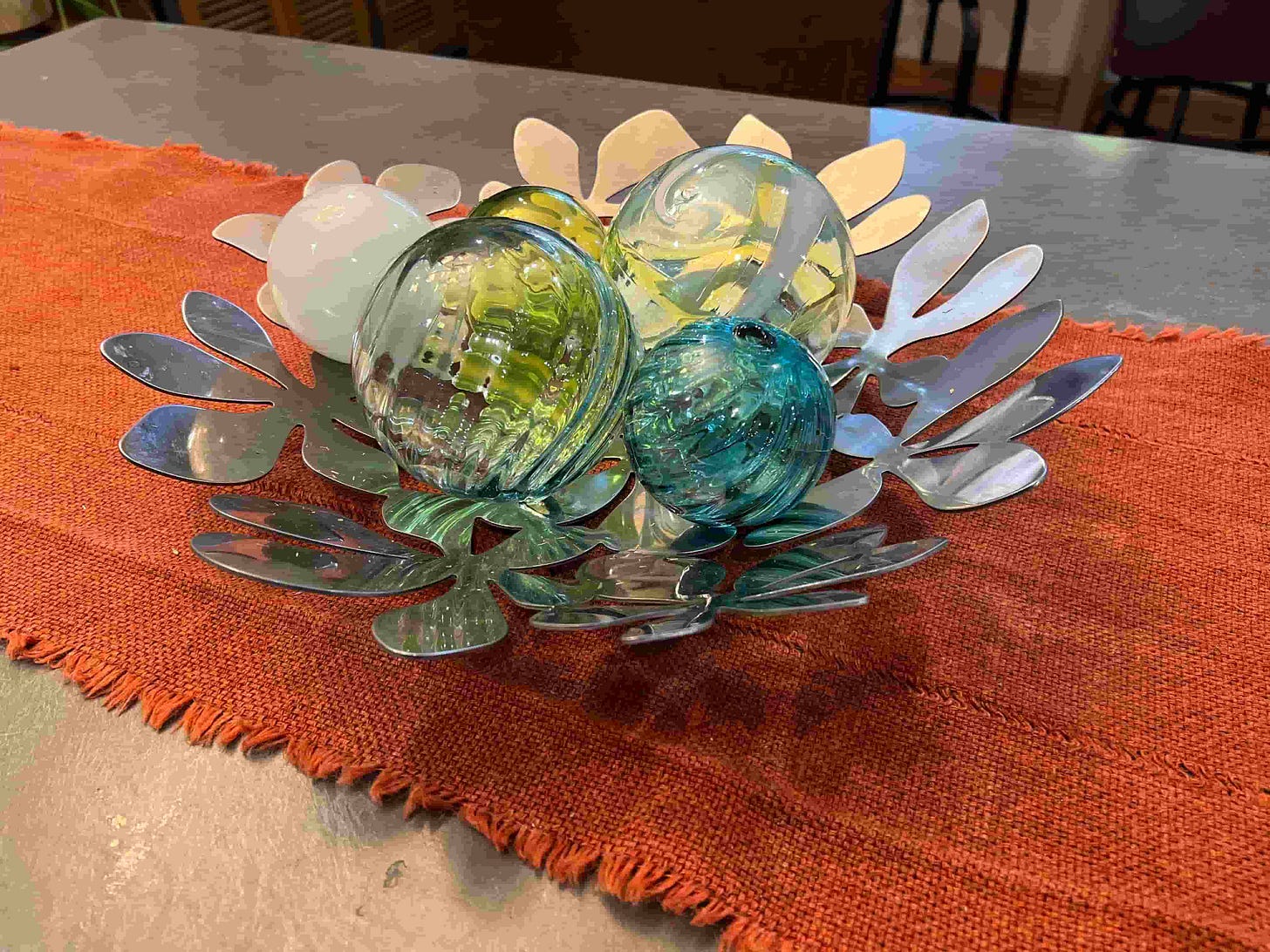photo of green and blue glass orbs in a metal basket on an orange table runner