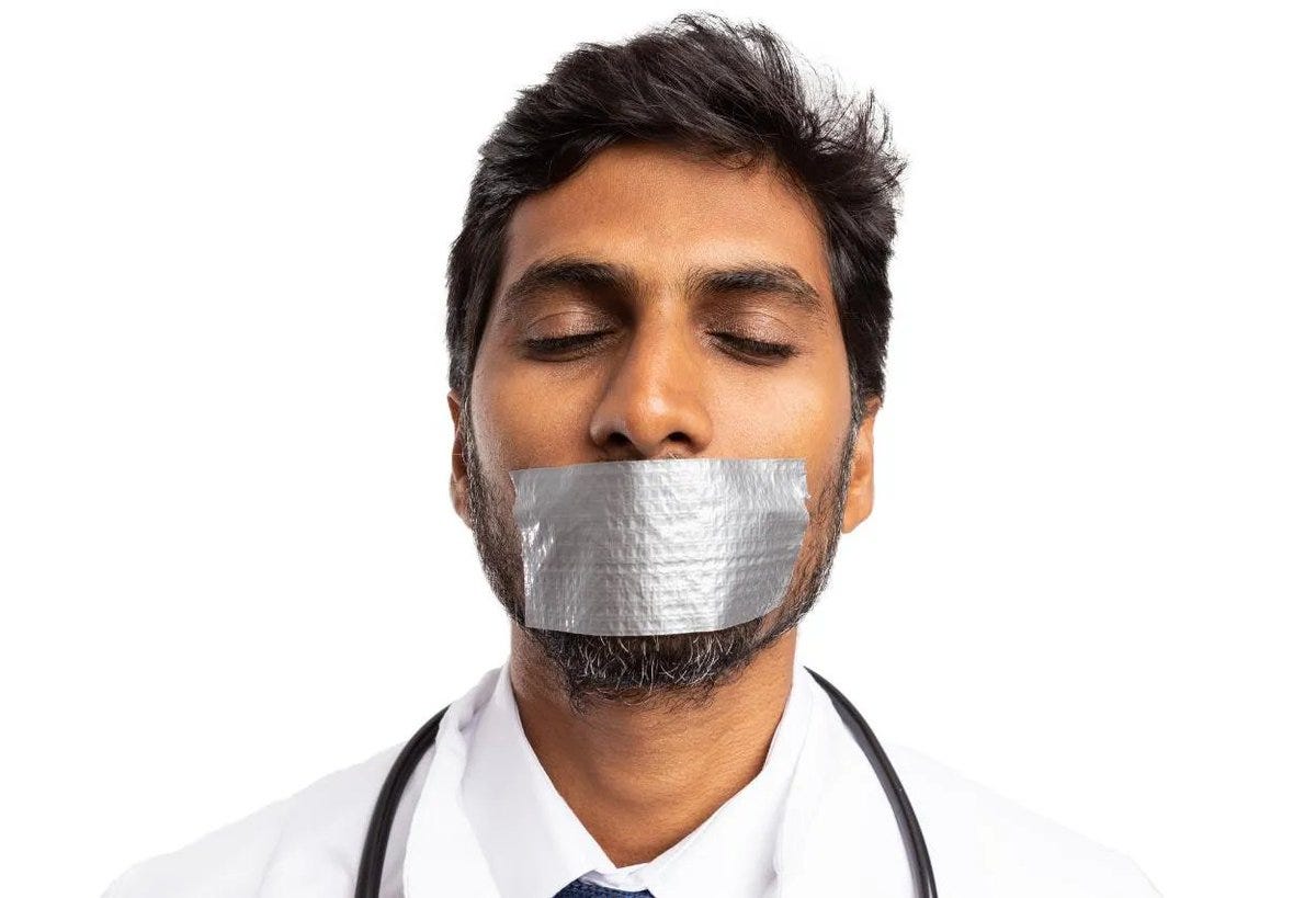 A man with dark hair and a beard, wearing a white coat and stethoscope, has silver duct tape covering his mouth.