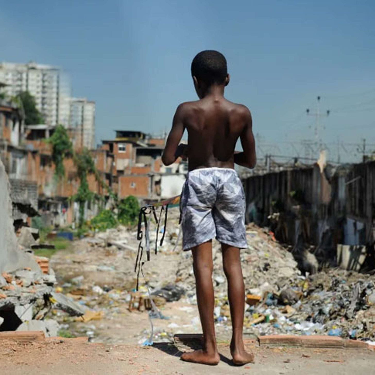 Photo of child in a favela with luxury apartments in the background.