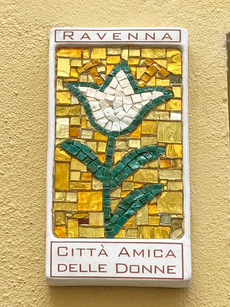 Three mosaic flower wall-plaques depicting a white lily, a white tulip and a poppy, with text declaring Ravenna to be a city friendly to women.