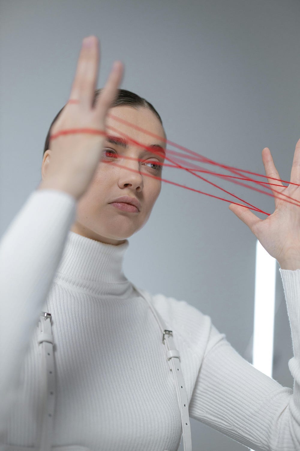 A woman in white attire artfully manipulates red threads on a gray background.