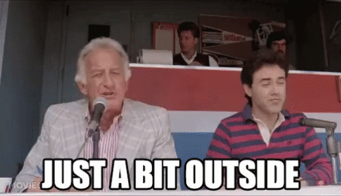 a man is sitting at a table talking into a microphone and the words just a bit outside are above him . a man is sitting at a table talking into a microphone and the words just a bit outside are above him .