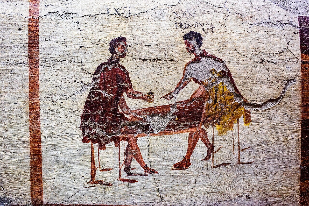 Two Roman men seated at a small table over a dice game, with Latin words painted above their heads, on a fresco from a Pompeii tavern