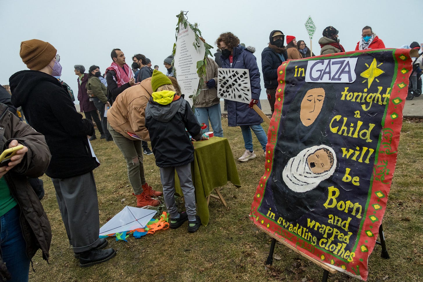 Protesters work at a craft table next to a sign that says "Tonight, in Gaza, a child will be born and wrapped in swaddling clothes."