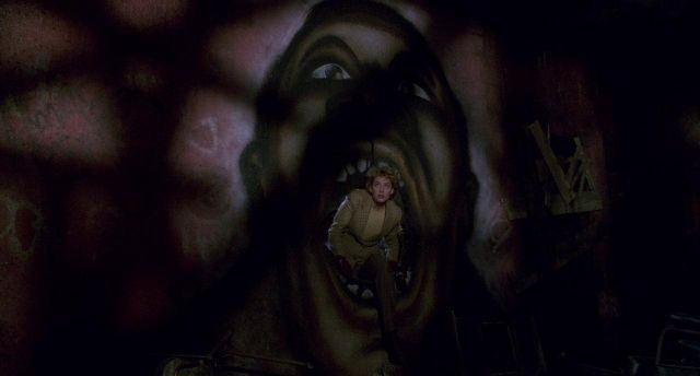 Virginia Madsen emerges from a hole in the wall, which is also a graffitti mouth of a black man Virginia Madsen emerges from a hole in the wall, which is also a graffitti mouth of a black man