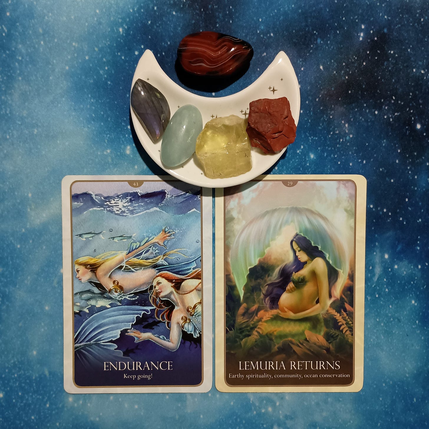 Care for Our Mother Earth ~ A Message From the Universe, two Oracle of the Mermaids cards and crystals on a starry blue background Care for Our Mother Earth ~ A Message From the Universe, two Oracle of the Mermaids cards and crystals on a starry blue background
