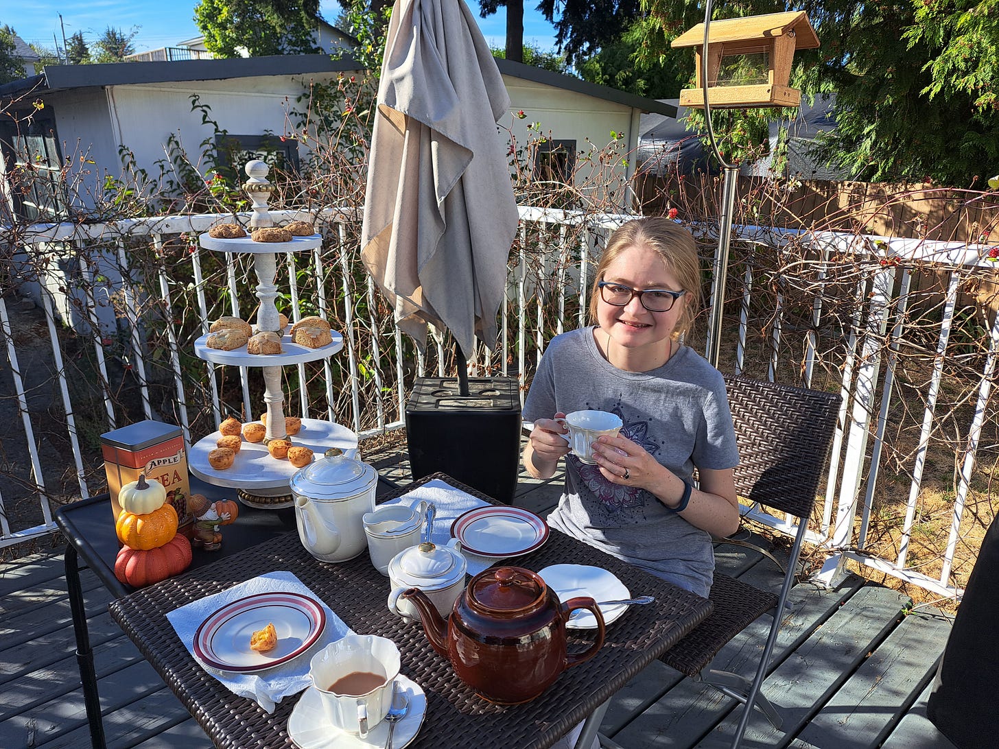 Me holding a cup of tea next to a tiered tray of my baking