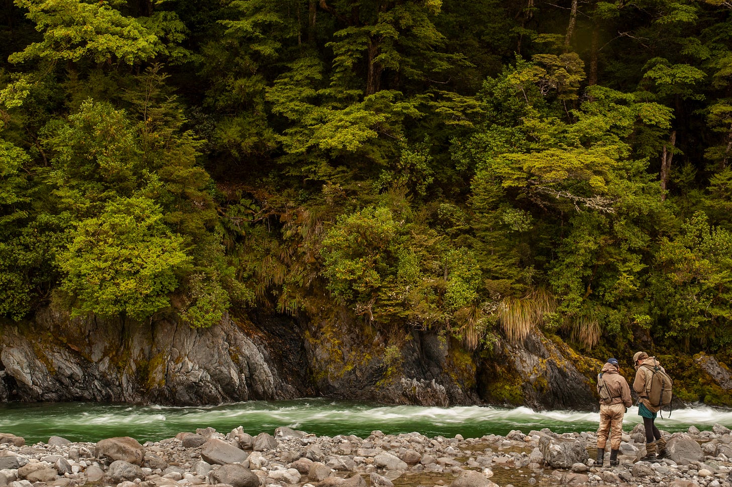 Two fly fisherman looking at flies along a river in New Zealand.