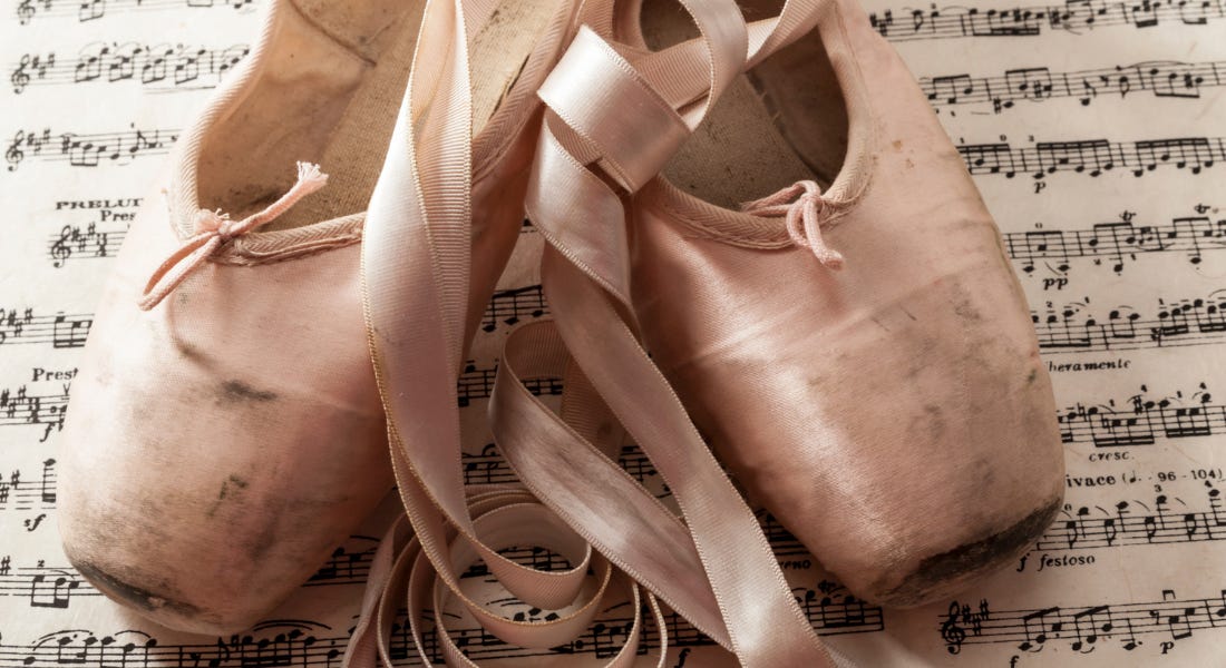 A pair of pale pink ballet slippers on top of a sheet of music A pair of pale pink ballet slippers on top of a sheet of music
