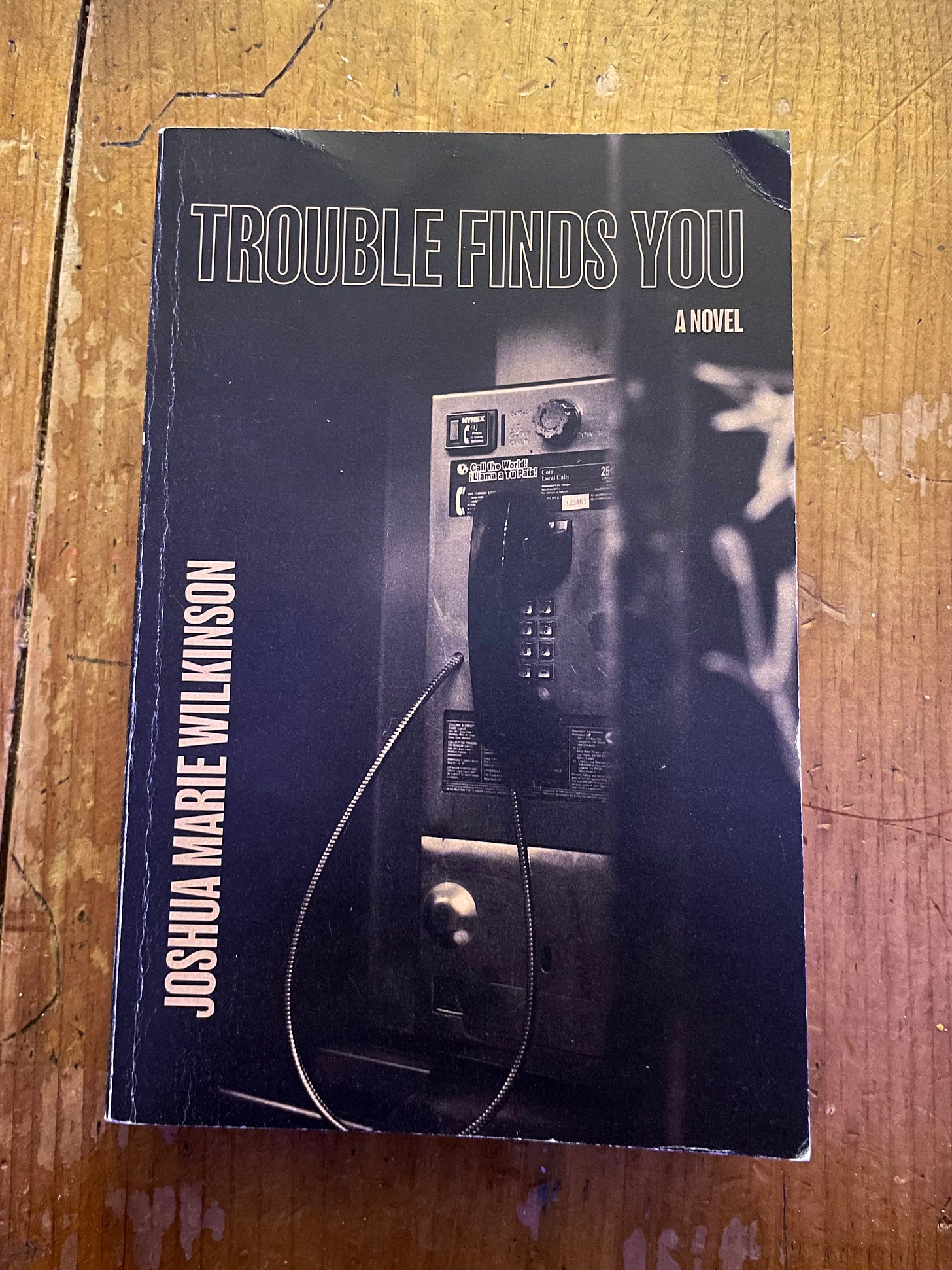 book on a wooden coffee table: 'Trouble Finds You' by Joshua Marie Wilkinson