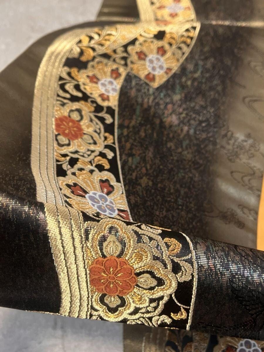 A figurative Nishijin maru obi depicting Heian court scenes, resting in its original paulownia storage box — calligraphy on the lid, gold thread catching the workshop light. The box is not packaging. It is part of the object’s provenance. A figurative Nishijin maru obi depicting Heian court scenes, resting in its original paulownia storage box — calligraphy on the lid, gold thread catching the workshop light. The box is not packaging. It is part of the object’s provenance.