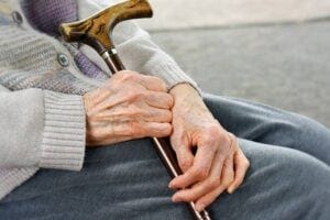 elderly man sitting on a bench with cane in hands