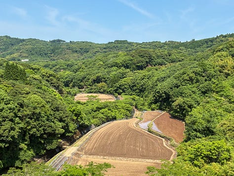 views of a deep-green reservoir surrounded by trees and fields far below on the other side of the dam