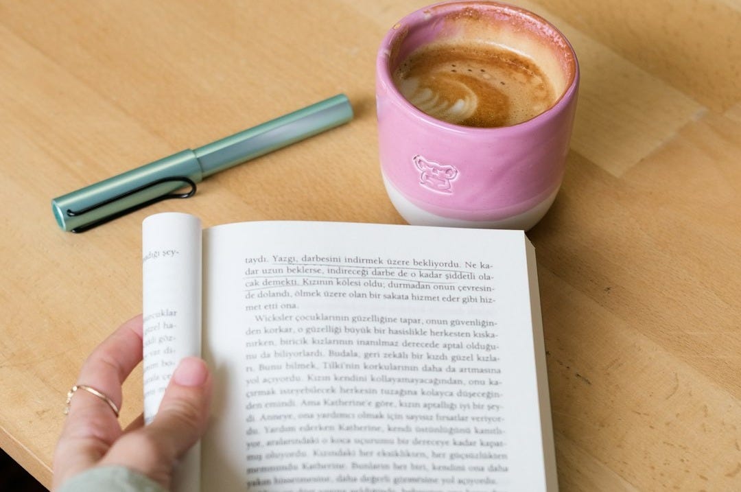 Person reading a book with coffee and pen.